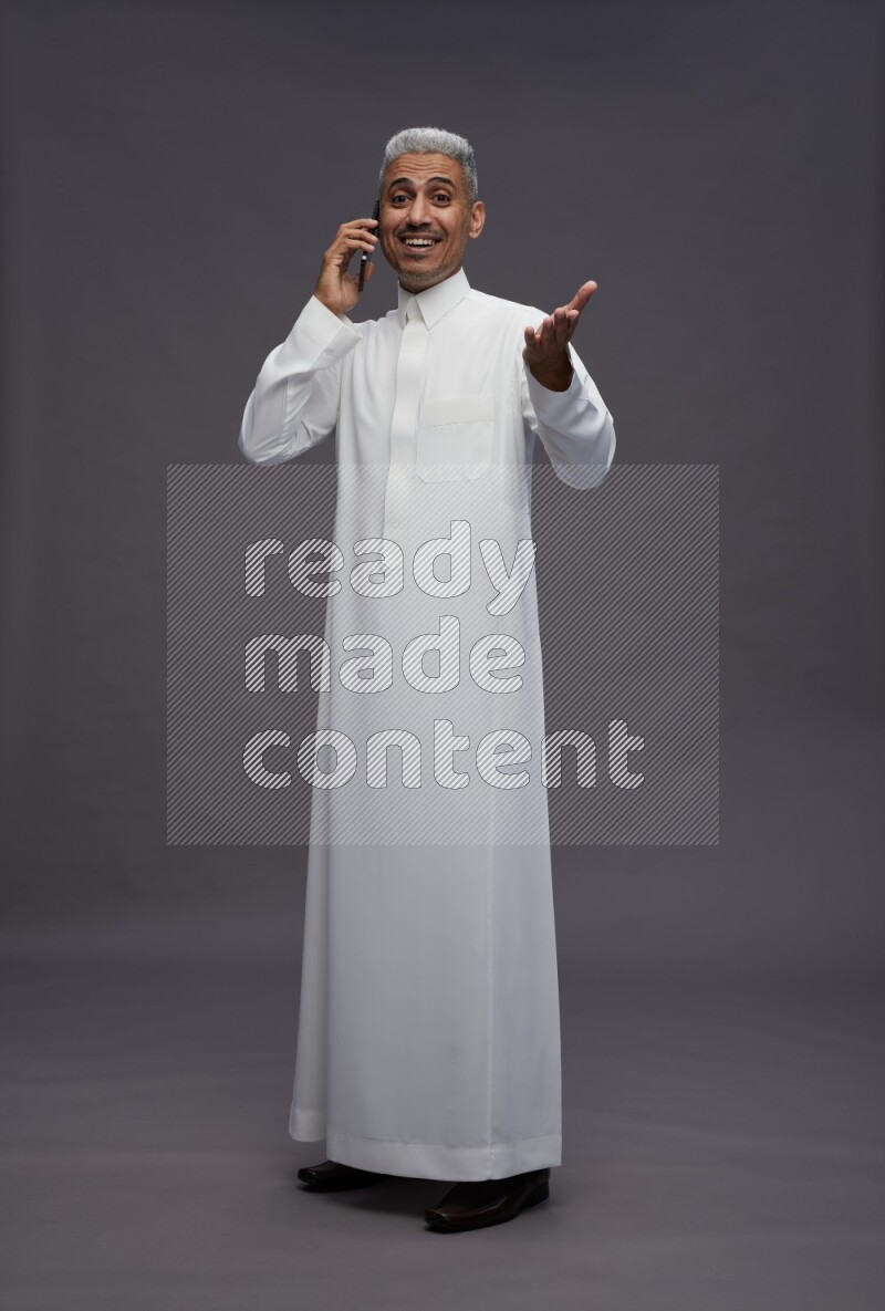 Saudi man wearing thob standing talking on phone on gray background