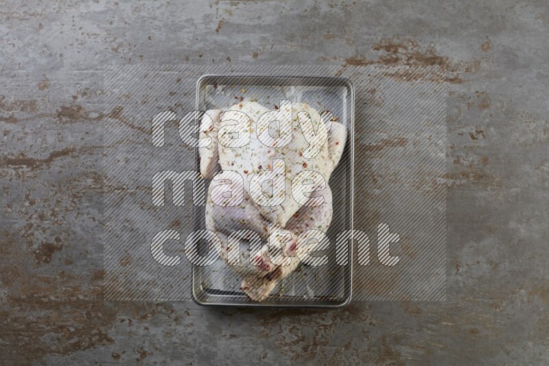 whole Raw chicken on a small oven trey direct on a rustic grey background