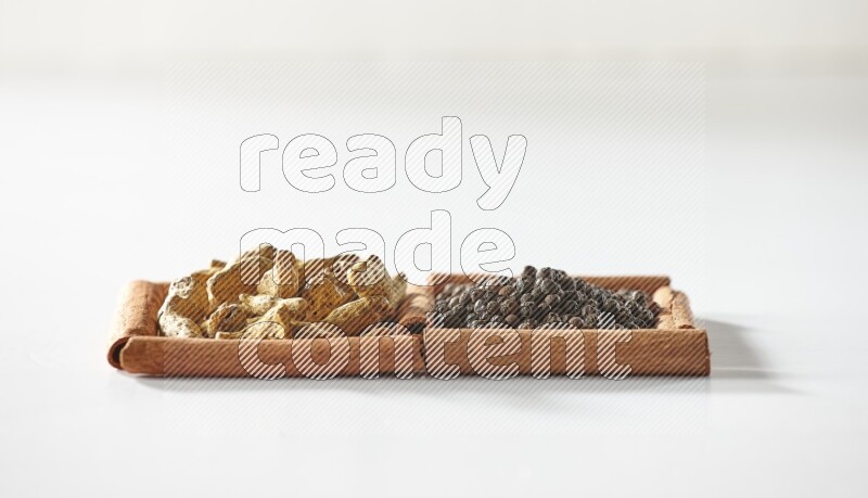 مربعان من أعواد القرفة ممتلئان بحبوب الفلفل الأسود وأصابع الكركم علي خلفية بيضاء