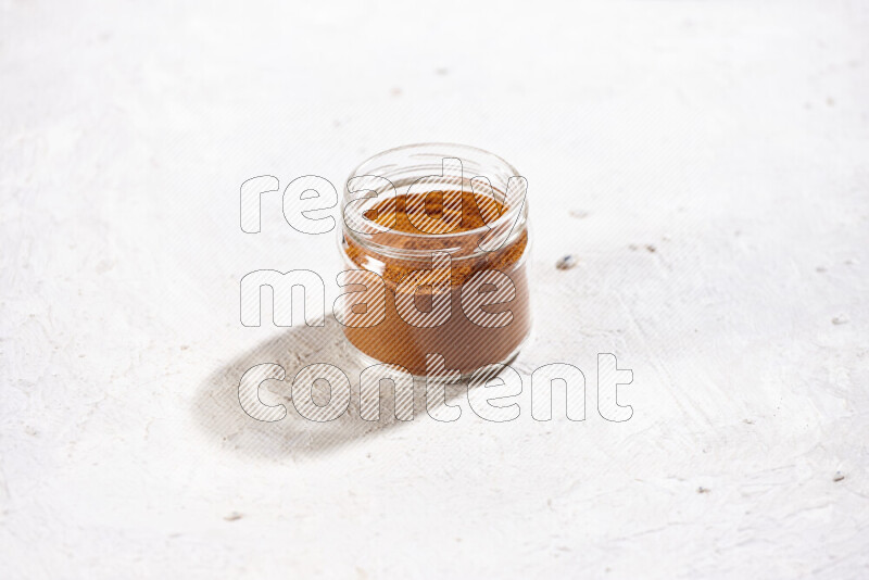 A glass jar full of ground paprika powder on white background