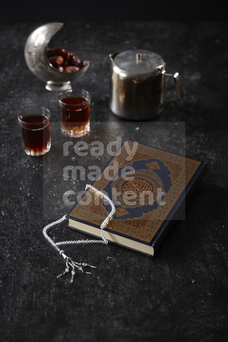 Moshaf with tea cups and prayer beads in a dark setup