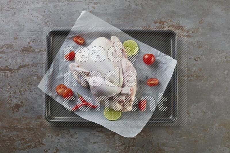 whole raw chicken on an oven trey direct on a rustic grey background