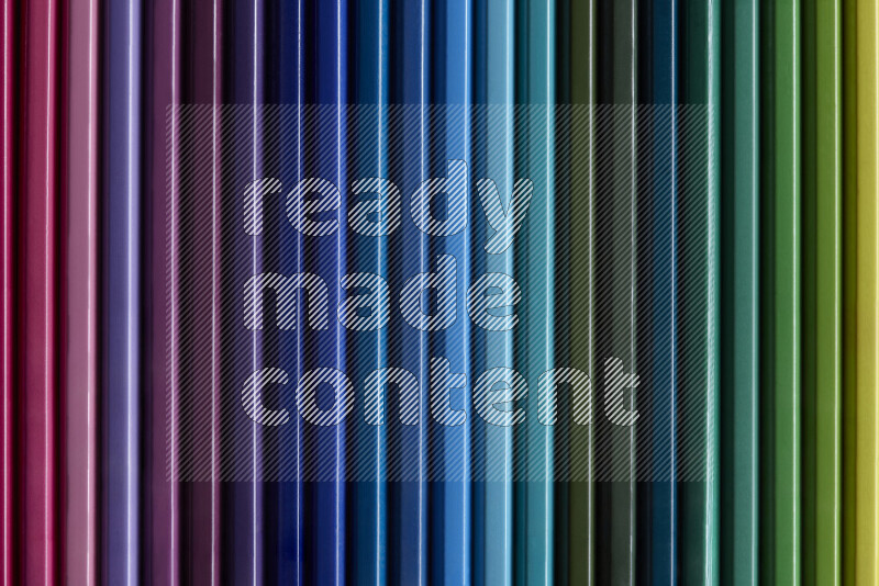 A collection of colored pencils arranged showcasing a gradient of different hues on grey background