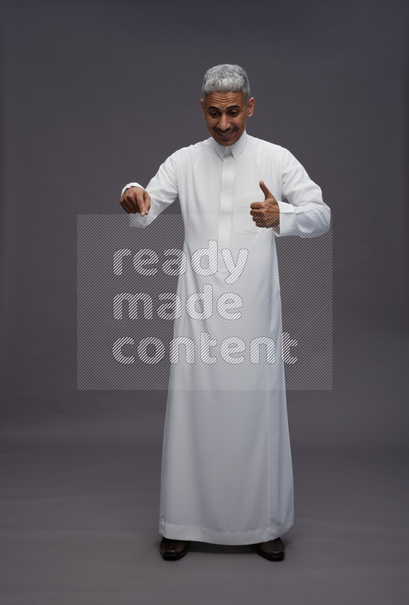Saudi man wearing thob standing interacting with the camera on gray background