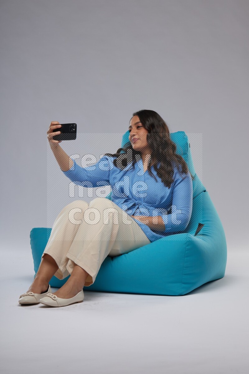 A woman sitting on a blue beanbag and taking selfie