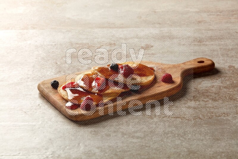 Three stacked mixed berries pancakes on a wooden board on beige background
