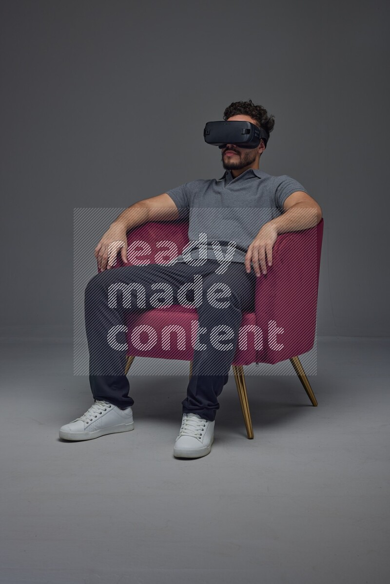 A man wearing casual and wearing VR while sitting on a burgundy chair eye level on a gray background