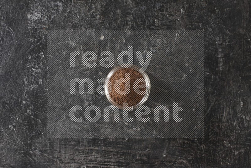 وعاء زجاجي ممتلئ ببودرة القرنفل على أرضية سوداء