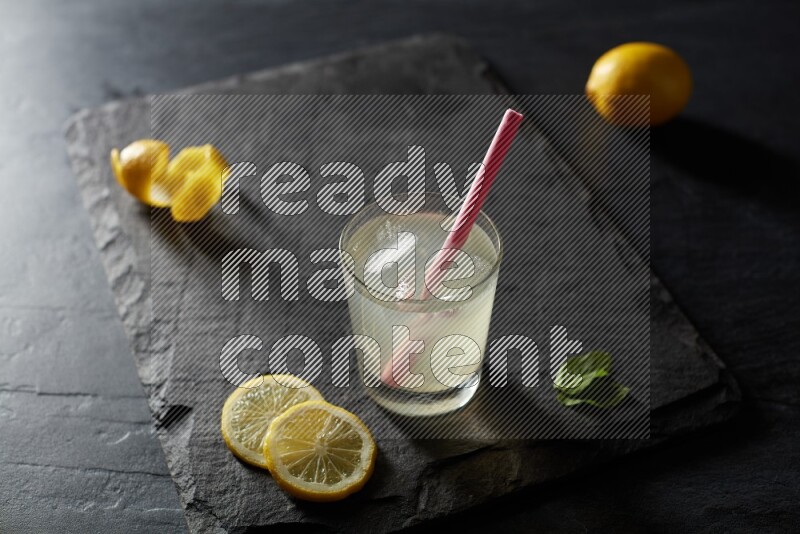 A glass of lemon juice with a straw on black background