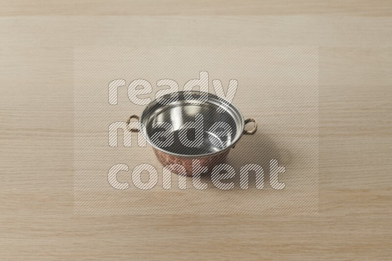 A small copper pot on light wooden background