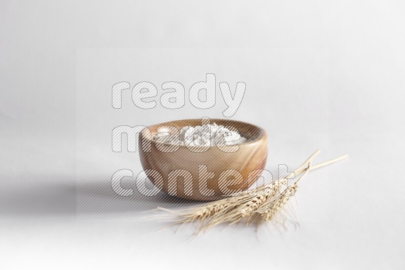 A wooden bowl full of flour with wheat stalks on white background