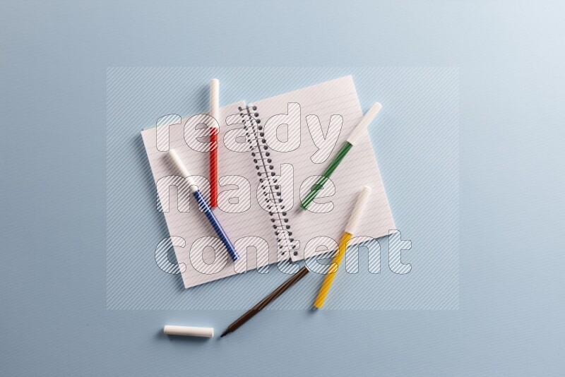 A blank open notebook with different school supplies on blue background