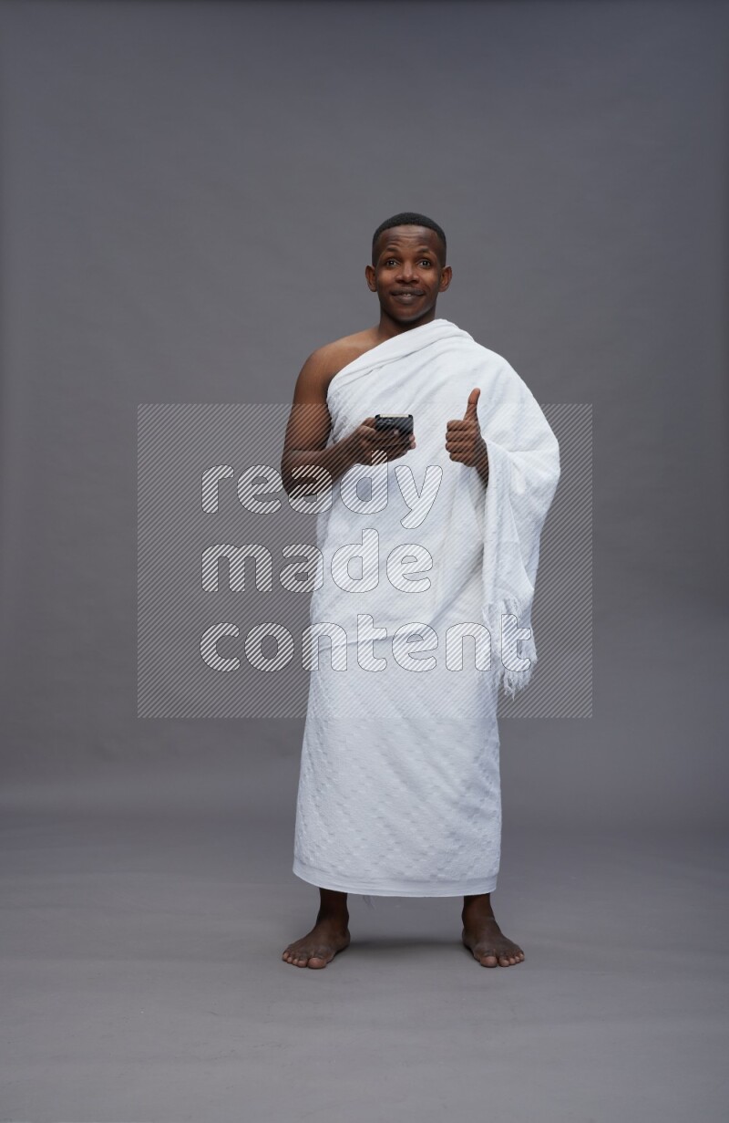 A man wearing Ehram Standing texting on phone on gray background