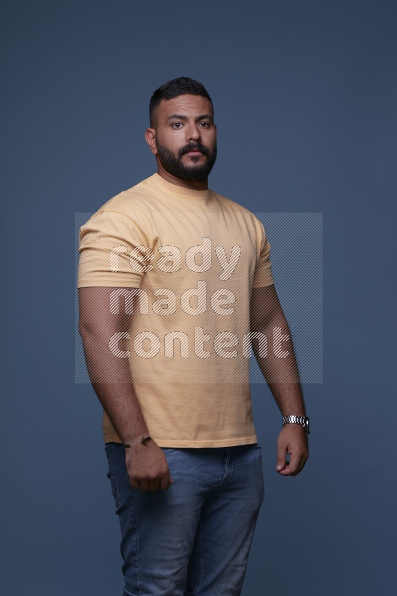 A man posing in a blue background wearing a yellow shirt