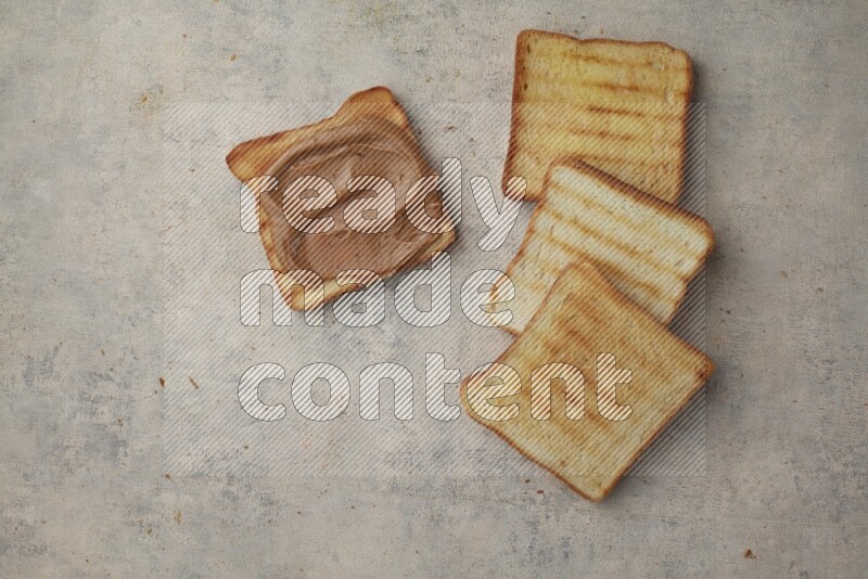 Creamy peanut butter on a toasted white toast and toasted white toast slices on a light blue textured background