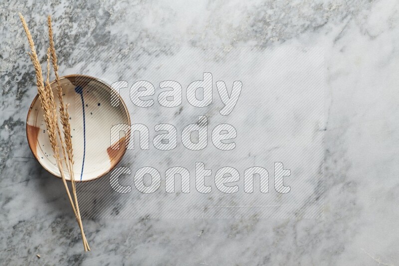 Wheat stalks on multicolored pottery plate on grey marble background