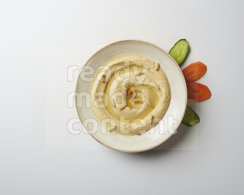 Hummus in a pottry plate garnished with pine nuts on a white background