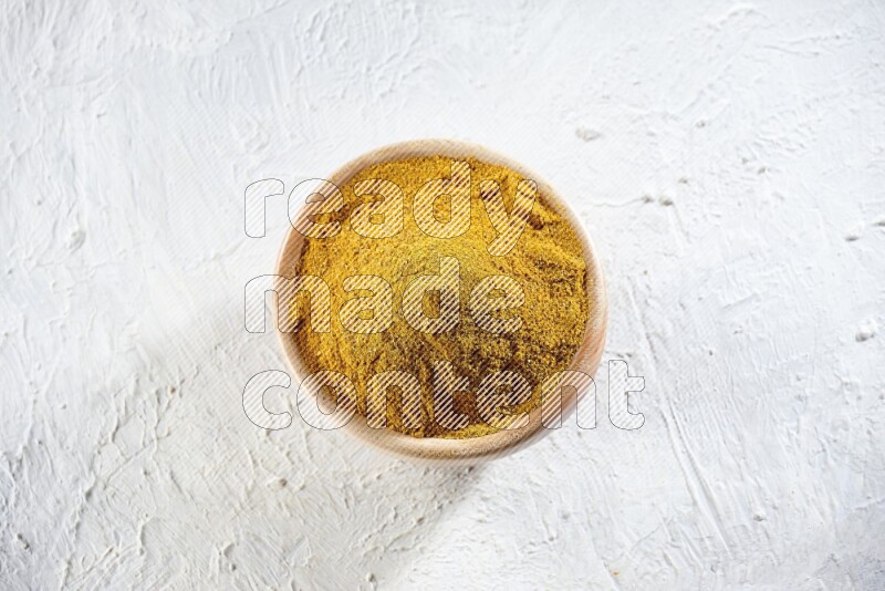 A wooden bowl full of turmeric powder on a textured white flooring