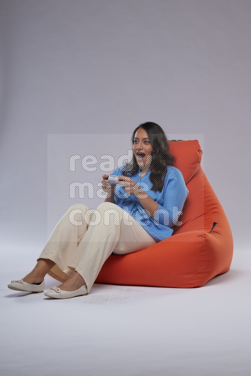 A woman sitting on an orange beanbag and gaming with joystick