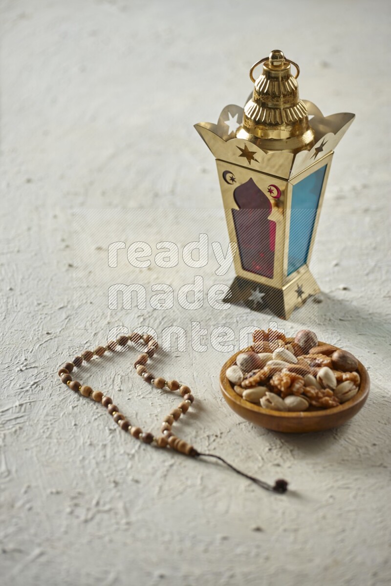 A golden lantern with different drinks, dates, nuts, prayer beads and quran on textured white background