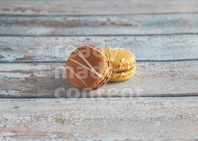 45º Shot of of two assorted Brown Irish Cream, and Yellow Piña Colada macarons on light blue background
