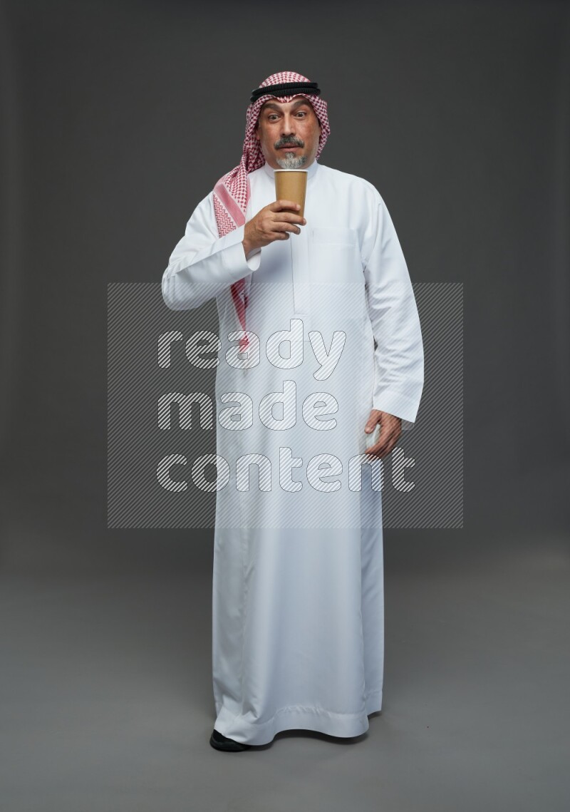 Saudi man with shomag Standing holding paper cup on gray background