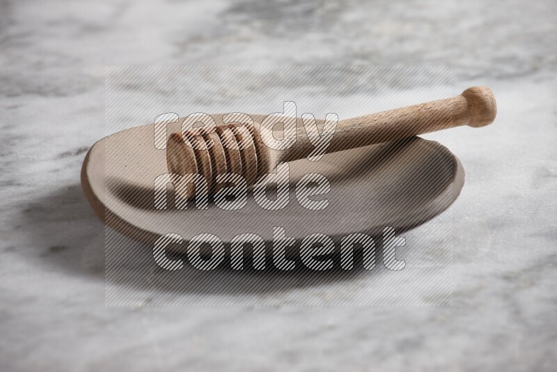 Multicolored pottery plate with wooden honey dipper in it on grey marble background
