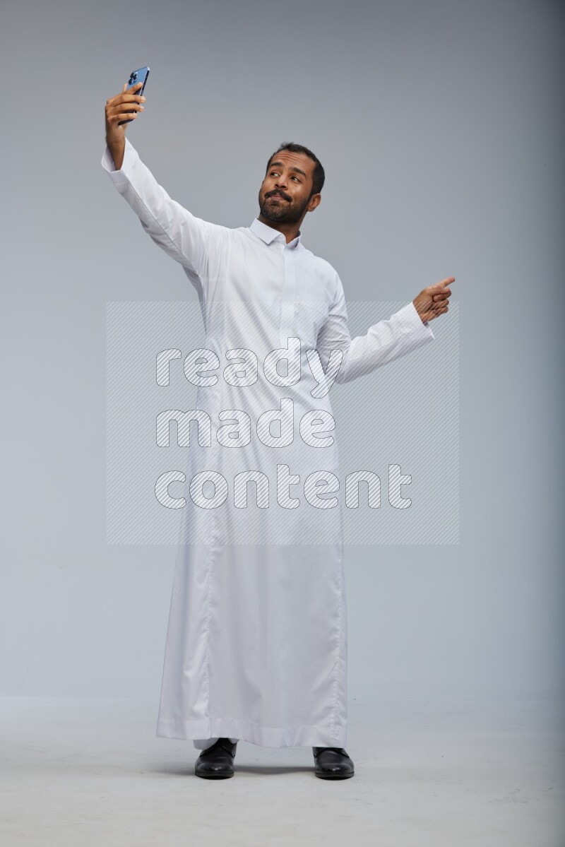 Saudi man wearing Thob standing taking selfie on Gray background