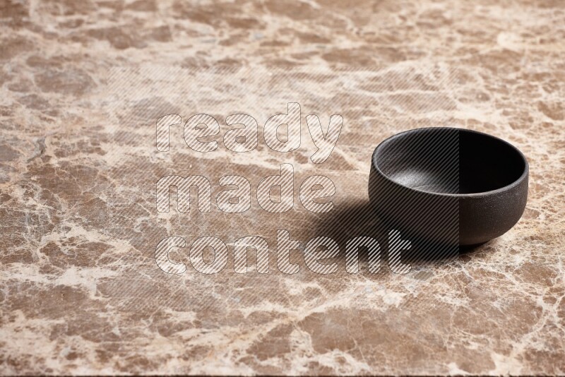 A black pottery bowl on beige marble background