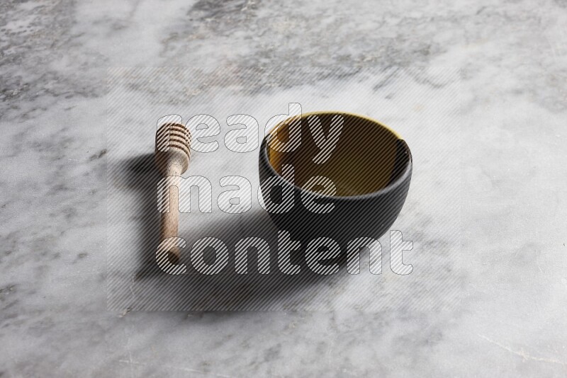 Multicolored pottery bowl with wooden honey dipper on the side on grey marble background