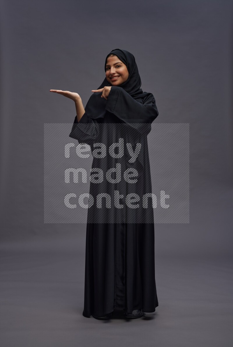 Saudi woman wearing Abaya standing interacting with the camera on gray background