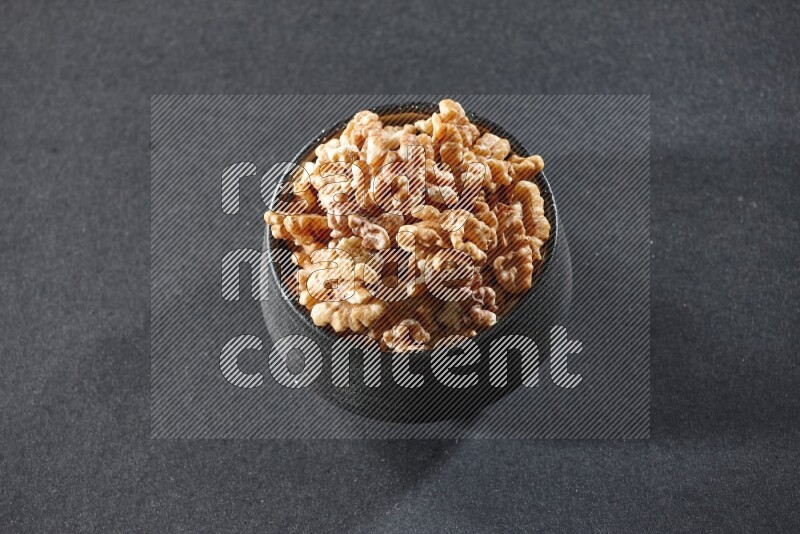 A black pottery bowl full of peeled walnuts on a black background in different angles
