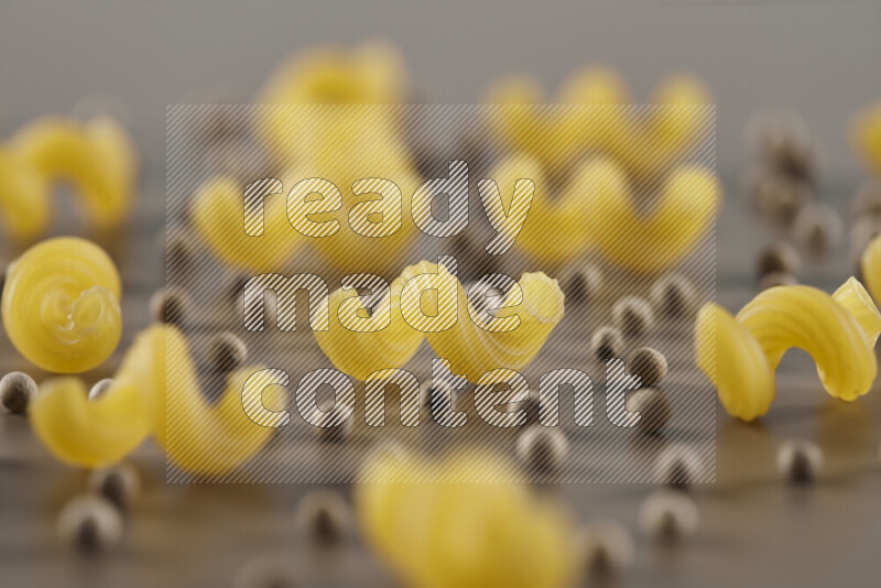 Raw pasta with different ingredients such as cherry tomatoes, garlic, onions, red chilis, black pepper, white pepper, bay laurel leaves, rosemary and cardamom on beige background
