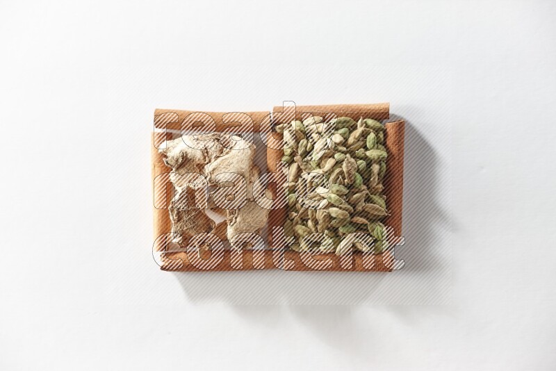 مربعان من أعواد القرفة ممتلئان بحبوب الهيل والزنجبيل المجفف علي خلفية بيضاء