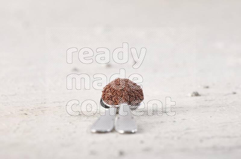 2 metal spoons full of garden cress seeds on a textured white flooring