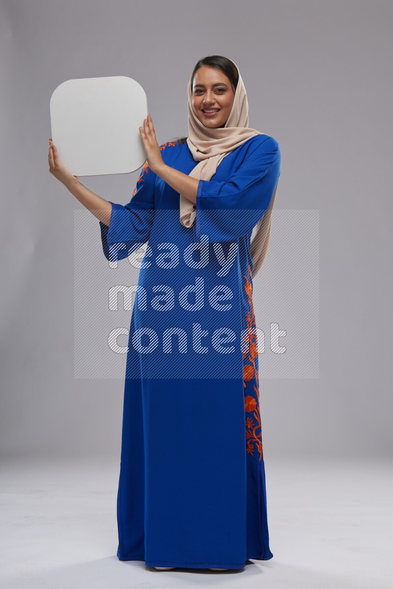 A Saudi woman standing wearing Jalabeya holding a social media sign