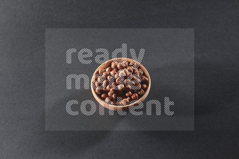 A wooden bowl full of peeled hazelnuts on a black background in different angles