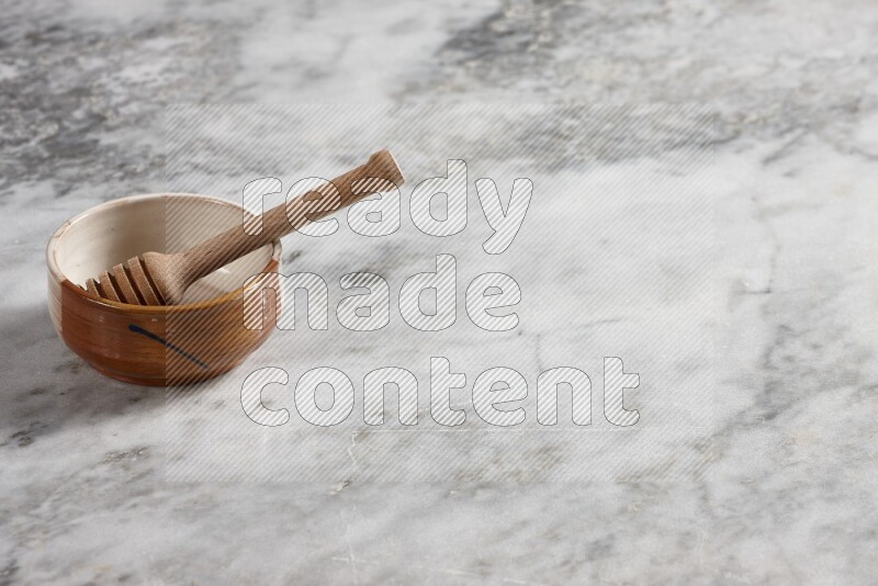 Multicolored pottery bowl with wooden honey dipper in it on grey marble background