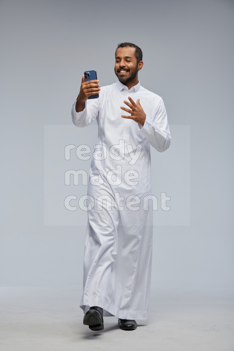 Saudi man wearing Thob standing taking selfie on Gray background