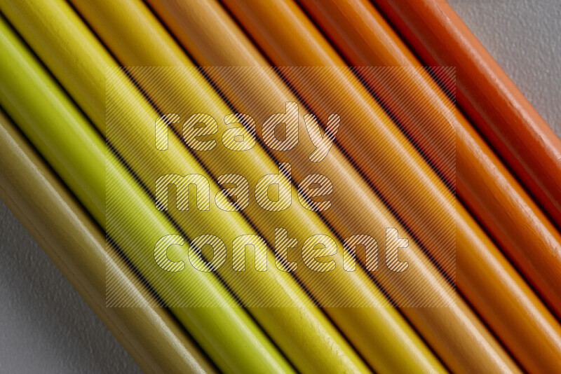 A collection of sharpened colored pencils arranged showcasing a gradient of yellow and orange hues on grey background