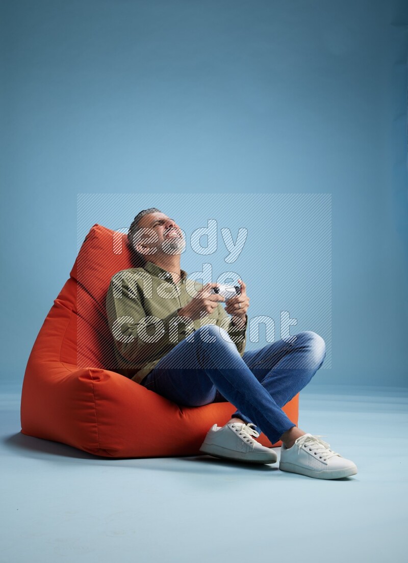 A man sitting on an orange beanbag and gaming with joystick