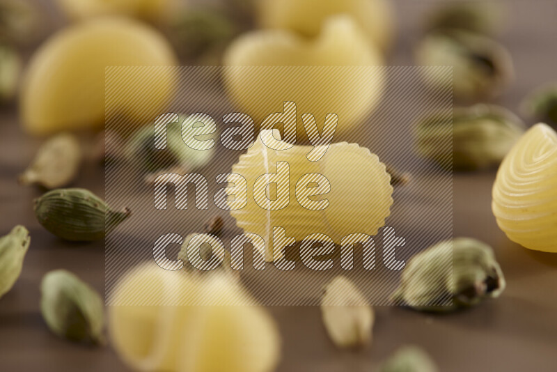 Raw pasta with different ingredients such as cherry tomatoes, garlic, onions, red chilis, black pepper, white pepper, bay laurel leaves, rosemary and cardamom on beige background
