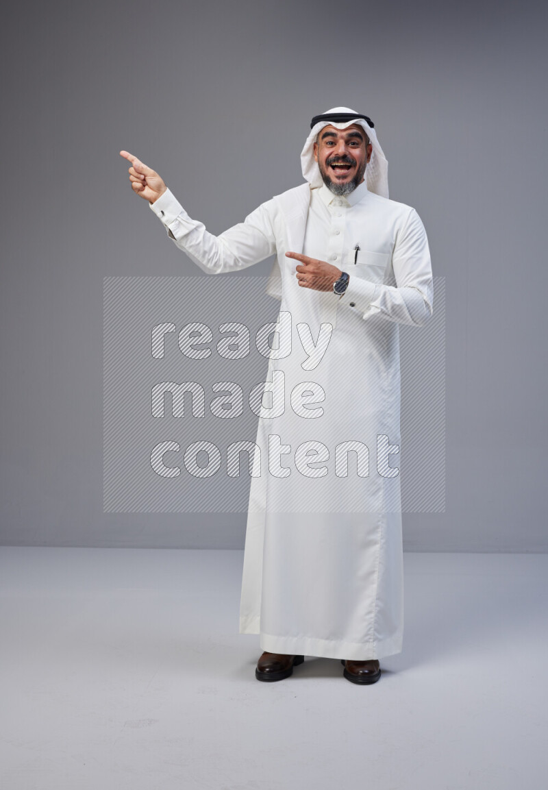 Saudi man Wearing Thob and white Shomag standing interacting with the camera on Gray background
