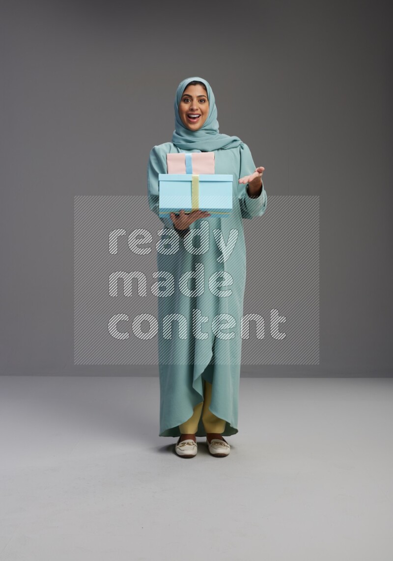 Saudi Woman wearing Abaya standing holding gift box on Gray background