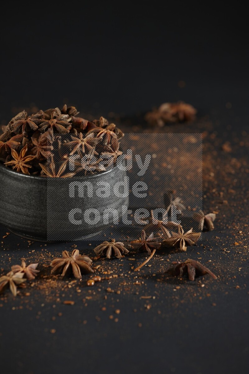 Star Anise in a black bowl with sprinkled anise on black flooring