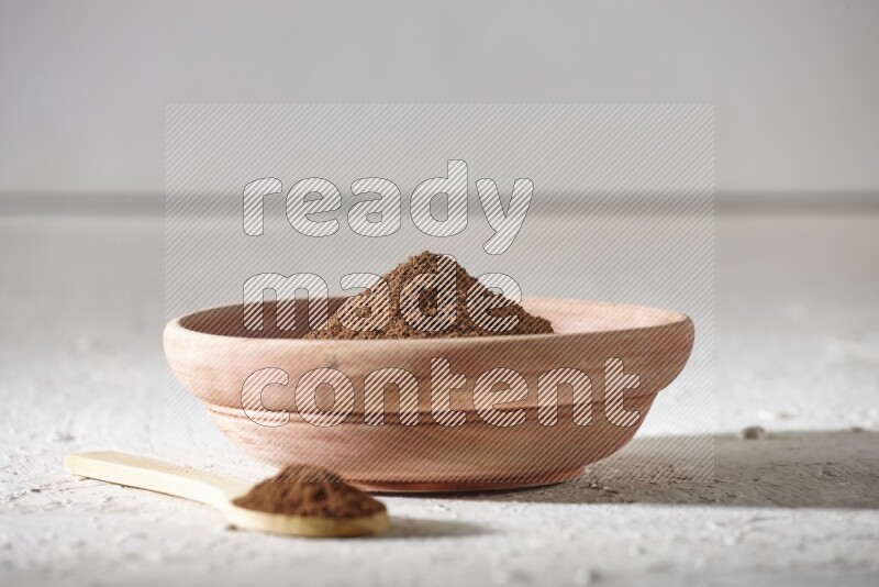 A wooden bowl and a wooden spoon full of cloves powder on a textured white flooring