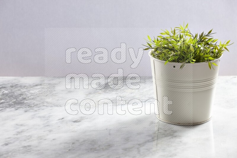 Green artificial plant in white pot on light grey marble background