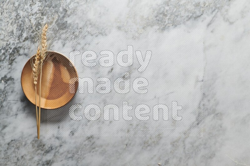 Wheat stalks on multicolored pottery plate on grey marble background