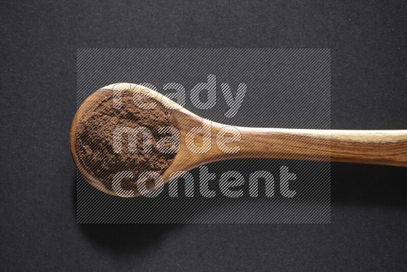 A wooden ladle full of cloves powder on a black flooring