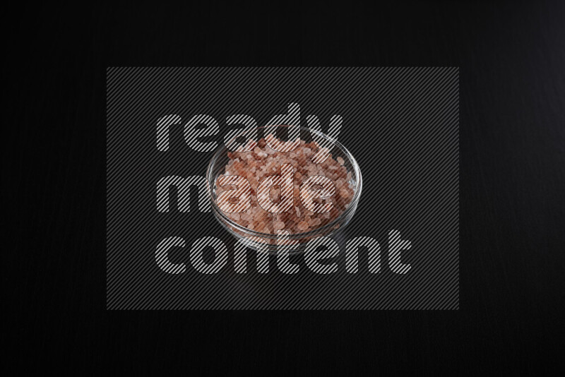 A glass bowl full of coarse himalayan salt crystals on black background
